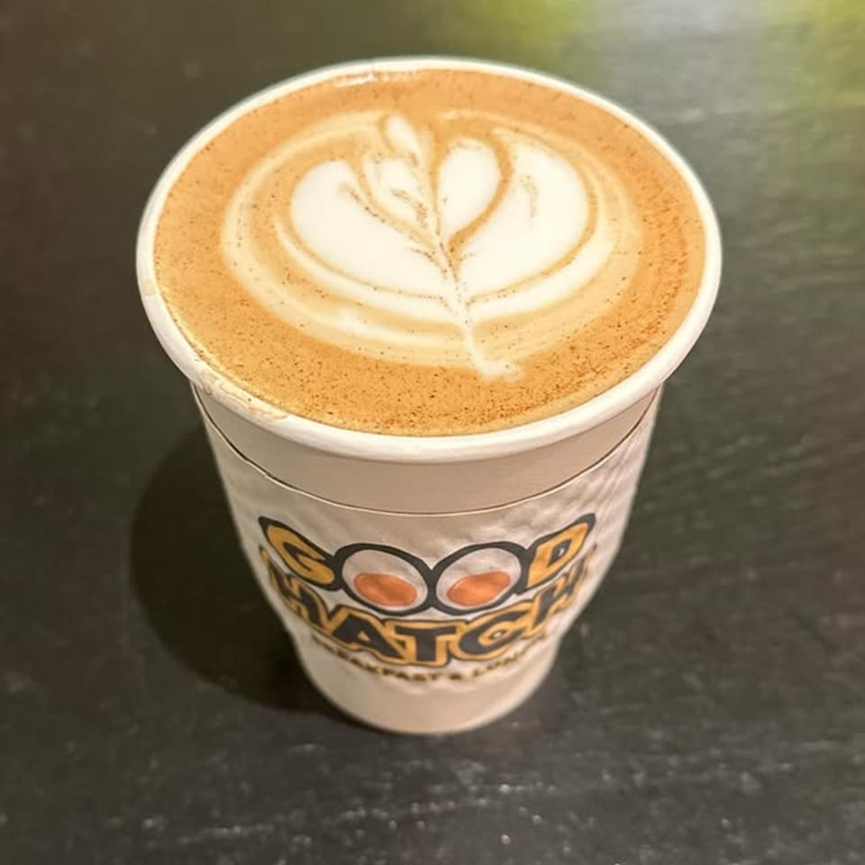 A Good Hatch branded coffee cup with latte art on a dark surface.