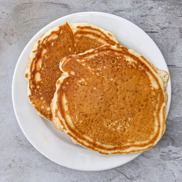 Two golden-brown pancakes on a white plate, ready to be served at Good Hatch.