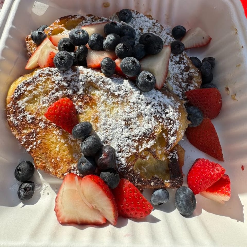 Good Hatch's French toast topped with powdered sugar, fresh blueberries, and sliced strawberries in a white container.