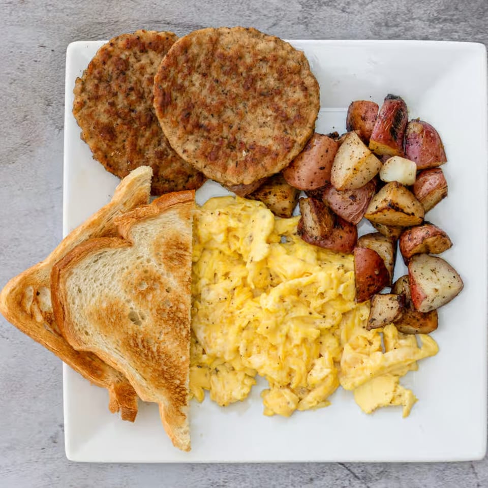 A Good Hatch breakfast plate with scrambled eggs, sausage patties, roasted potatoes, and toast.